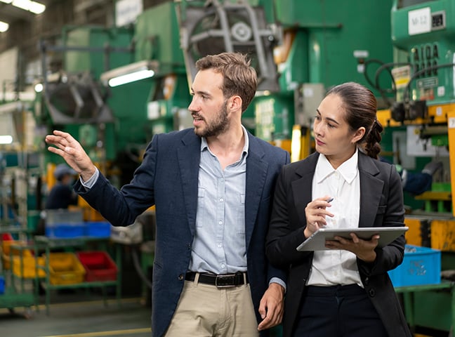 Two engineering professionals, a man and a woman, in conversation while walking in a factory.