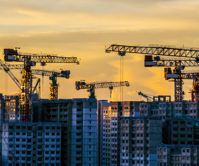 Sky-rise buildings under construction with cranes in the background during sunset.
