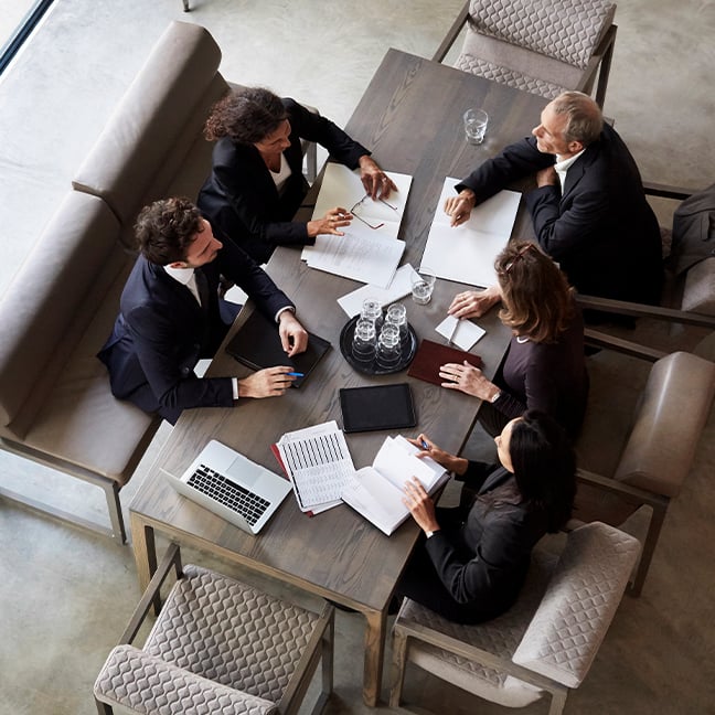 Groupe diversifié de professionnels assistant à une réunion et examinant des documents à une grande table.